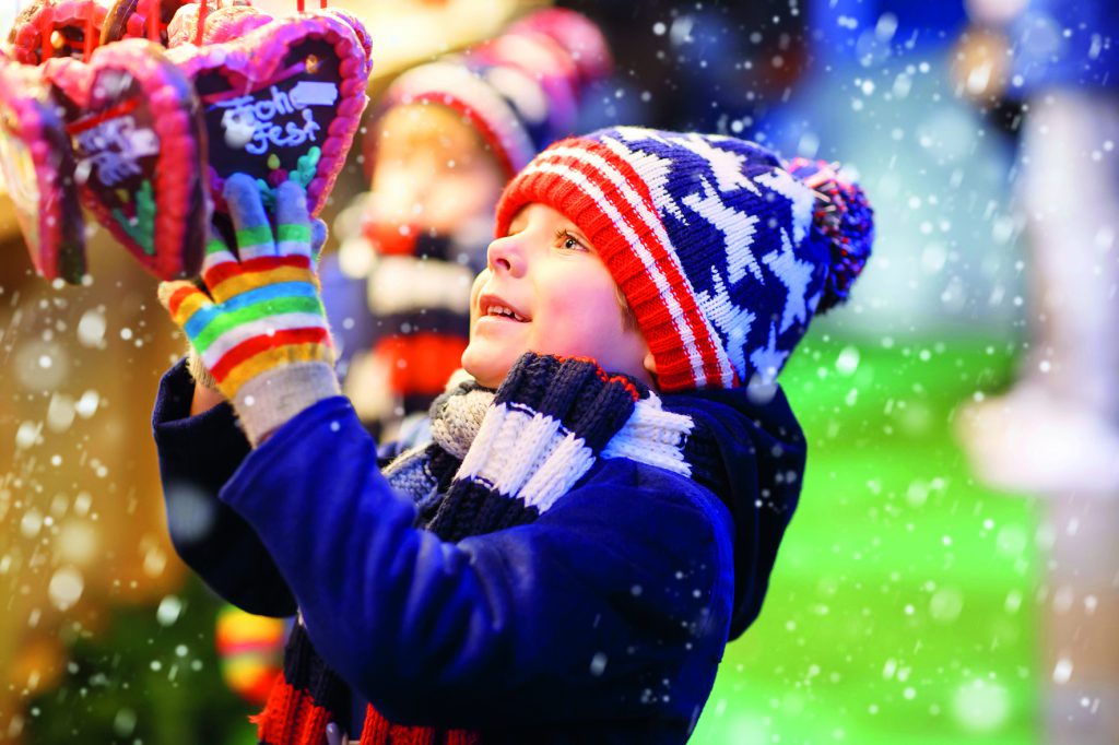 Little cute kid boy happy about gingerbread cookies hearts. Happy child on Christmas market in Germany. Traditional leisure for families on xmas